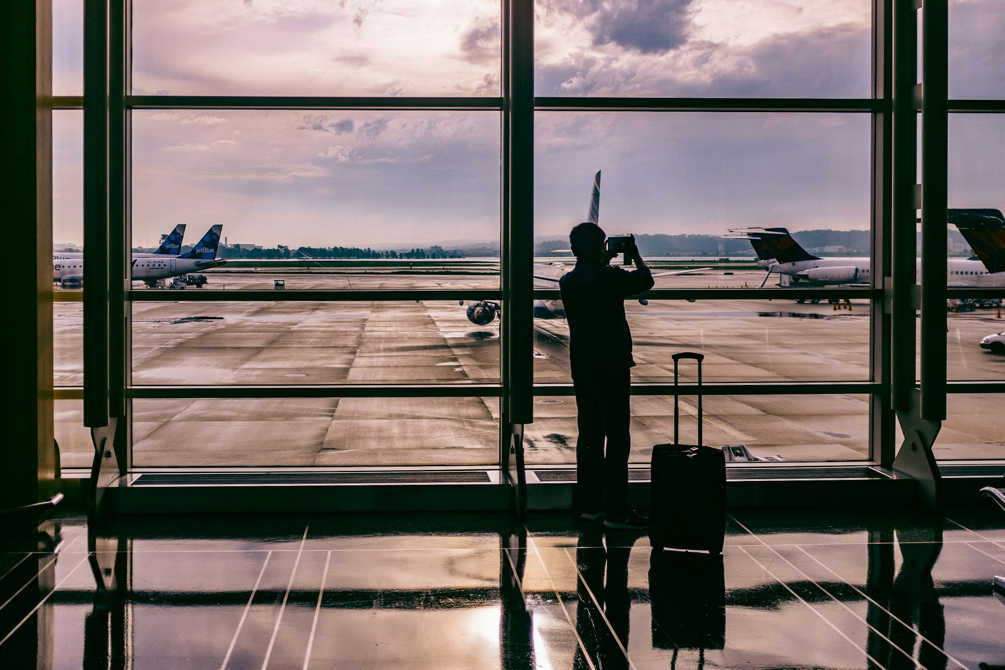A traveller watching aircraft from an airport terminal window at dusk